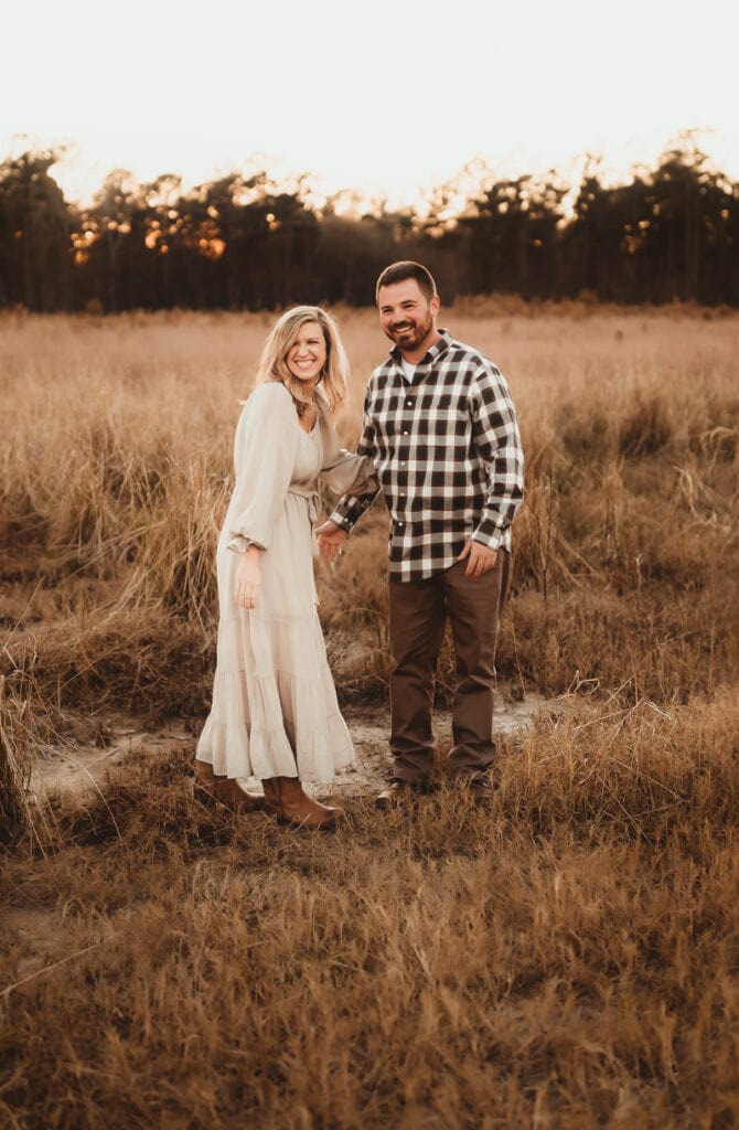 Family Photographer, a couple, husband and wife, hold hands in a dry field